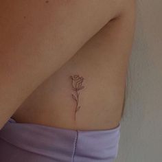 a woman's stomach with a single flower tattoo on her left side ribcage