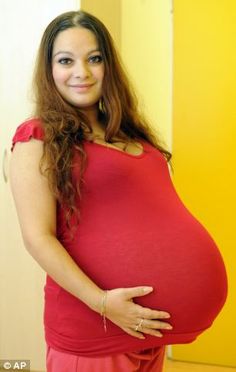 a pregnant woman in a red dress poses for the camera while holding her belly up