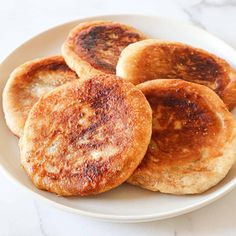 four pancakes on a white plate sitting on a marble counter top, ready to be eaten