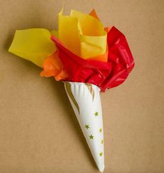 a white vase with red, yellow and orange flowers in it on a brown surface