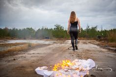 a woman walking down a dirt road next to a fire