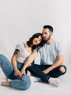 a man and woman sitting next to each other on the floor in front of a white background