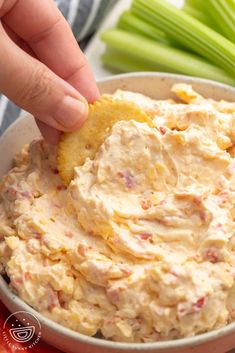 a hand dipping a cracker into a bowl of dip