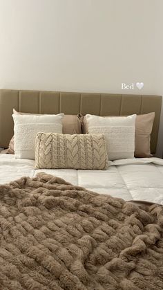 a bed with two pillows on it and a blanket over the headboard, in front of a white wall