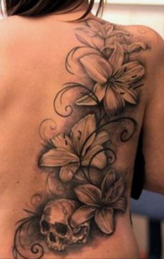 a skull and flowers tattoo on the back of a woman's shoulder, with an artistic design