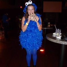 a woman dressed as cookie monster holding a cookie in front of her face while standing next to a table