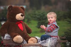 a young boy sitting on top of a wooden crate next to a large teddy bear