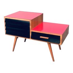 a pink and black side table with two drawers on one end, and a drawer on the other