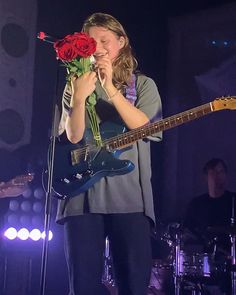 a woman holding a rose while standing in front of a guitar and microphone on stage