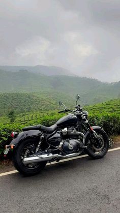 a motorcycle is parked on the side of the road in front of some bushes and mountains