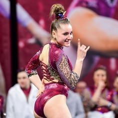 a woman in a red leotard is standing on one leg with her hand up