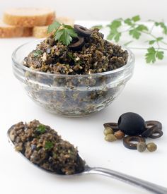 a glass bowl filled with food next to bread and parsley on a white surface