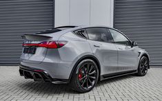 the rear end of a silver sports car parked in front of a garage door with roller shutters