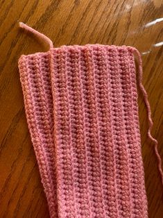 a pink crocheted piece of cloth on a wooden table next to a pair of scissors