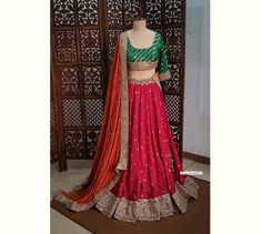 Made to Order/Measurement/Custom Order Lehenga - Color : Red, Orange and Green - Fabric : Embroidered Upada Silk with Rich Border - Fully flared paneled lehenga  - Princess Cut Padded Green Brocade Silk Blouse with borders - Orange Georgette Dupatta with motifs and border - Can Can attached - Drawstring closure with Tassels PLEASE NOTE: BUYERS ARE RESPONSIBLE FOR ANY CUSTOMS AND IMPORT TAXES THAT MAY APPLY. Fabric Care : Dry Clean Only Disclaimer: Please note the photographs are taken by mobile Fitted Red Lehenga With Gota Work, Red Banarasi Silk Sets With Gota Work, Fitted Red Banarasi Silk Sharara, Fitted Red Choli With Gota Work, Designer Red Banarasi Silk Choli, Fitted Red Anarkali Set In Raw Silk, Fitted Red Raw Silk Lehenga, Orange Lehenga, Silk Lehenga Choli