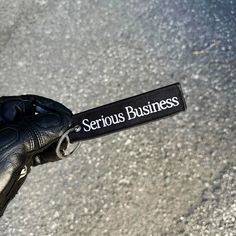 a person wearing black leather gloves and holding a name tag in their left hand with the word serious business written on it