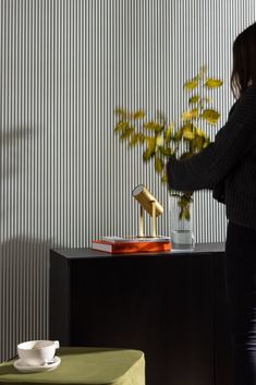 a woman standing next to a table with a vase on it