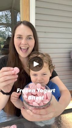 a woman holding a baby in front of a glass bowl filled with marshmallows