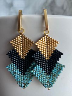 two pairs of earrings with gold and black beads on them, hanging from a white cup