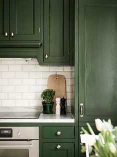 a kitchen with green cabinets and white tile backsplash, potted plants on the counter