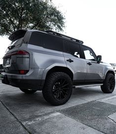 the rear end of a silver suv parked on top of a parking lot next to a tree