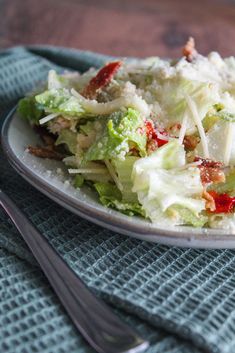 a white plate topped with a salad covered in lettuce and bacon next to a fork