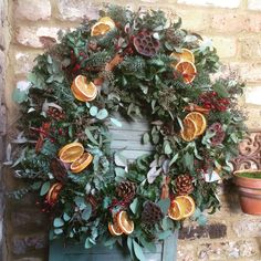 a wreath with oranges and pine cones on it sitting in front of a brick wall