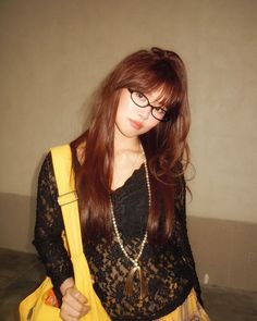 a woman with long red hair and glasses holding a yellow purse