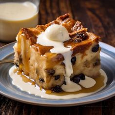 a piece of bread pudding with blueberries and cream on a plate next to a glass of milk