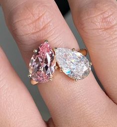 a woman's hand with two engagement rings on top of her finger and the ring has three pear shaped diamonds in it