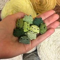 a hand is holding small crocheted animals in front of balls of yarn and yarn