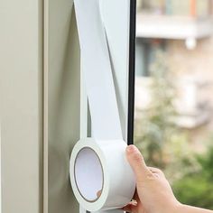 a person is holding a roll of tape near a window with the door handle open