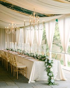 a long table is set up with white linens and greenery for an elegant wedding reception