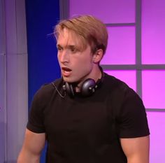 a man with headphones on his ears is making a face while standing in front of a purple wall