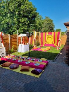 an outdoor party setting with colorful decorations and tables on the grass, in front of a fence