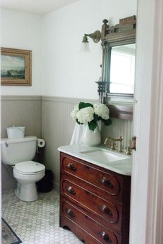 a white toilet sitting next to a wooden dresser in a bathroom under a mirror with flowers on it