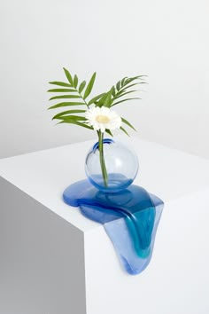 a blue vase with a flower in it on top of a white table and some green leaves