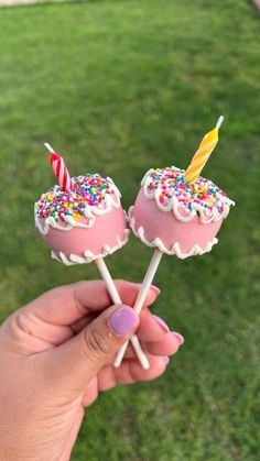 someone holding two cake pops with sprinkles and a candle on them in their hand