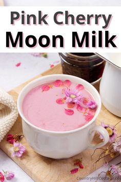 pink cherry moon milk is in a white bowl on a cutting board with flowers around it