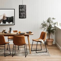 a dining room table with chairs around it and a cow print on the wall behind it