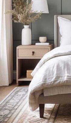 a bed with white linens and pillows in a bedroom next to a lamp on a nightstand