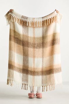 a tan and white plaid blanket with fringes hanging from it's end, next to pink slippers