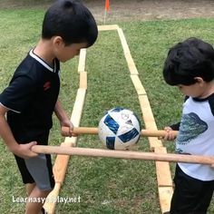 two young boys playing with a soccer ball on a wooden frame in the grass outside