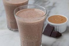 two glasses filled with chocolate milkshakes on top of a marble counter next to a small bowl of peanut butter