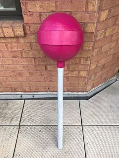 a large pink ball sitting on top of a white pole next to a brick wall