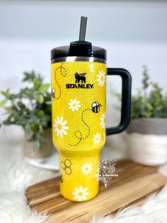 a yellow travel mug with black lid and handle sitting on a wooden tray next to some plants