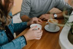 two people sitting at a table with cups of coffee in front of them and one person holding the other's hand