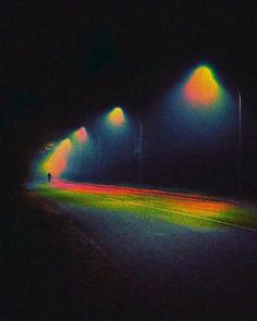 an empty street at night with lights shining on the road and people walking in the distance