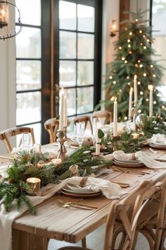 the table is set for christmas dinner with candles and greenery in front of it