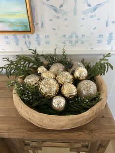 a wooden bowl filled with gold ornaments on top of a table next to a painting